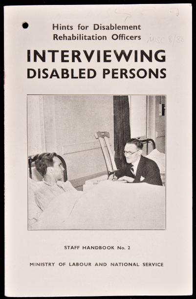 Black and white booklet with a picture on the cover of a man in a hospital bed, with another man in a suit sitting next to him, under the title 'Interviewing Disabled Persons.'
